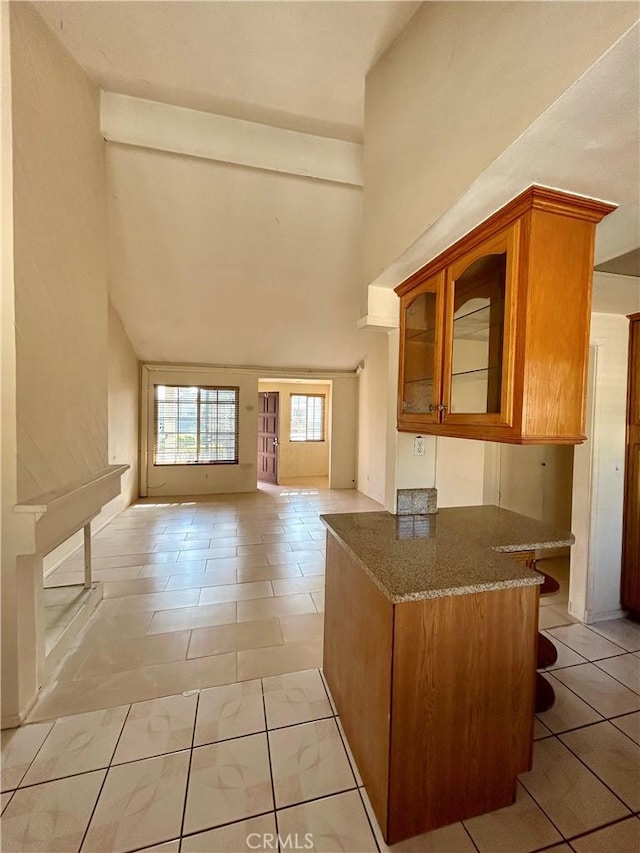 kitchen featuring glass insert cabinets, brown cabinets, a high ceiling, and dark stone countertops