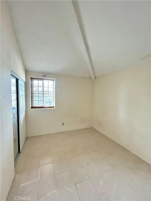 empty room with vaulted ceiling with beams and light tile patterned floors