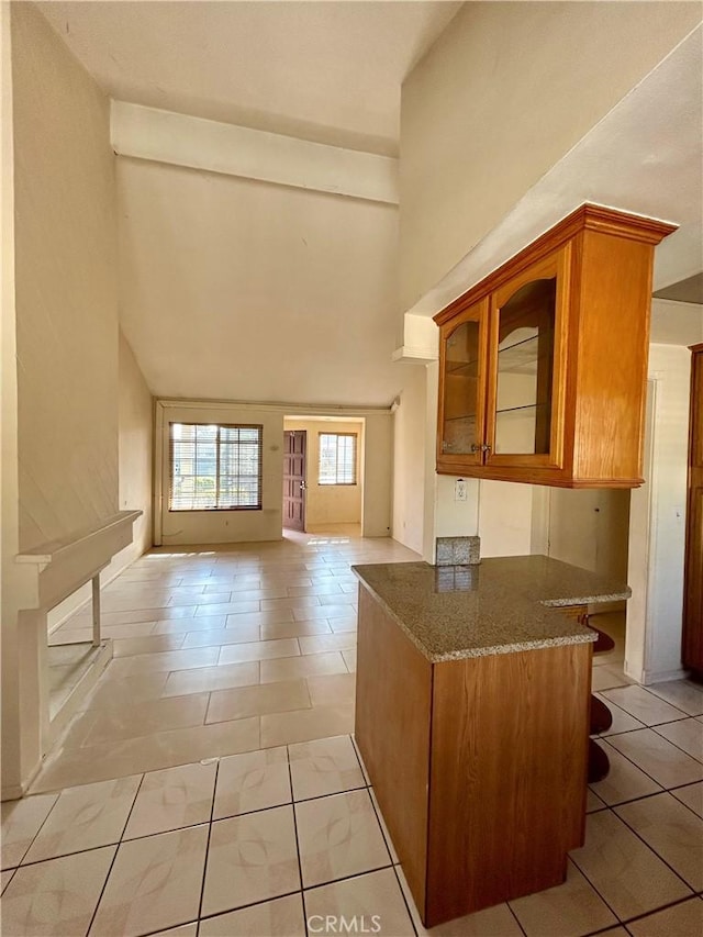 2635 W Monte Carlo Dr Unit 42, Santa Ana, CA 92706 - kitchen featuring a towering ceiling, dark stone countertops, glass insert cabinets, brown cabinetry, and open floor plan