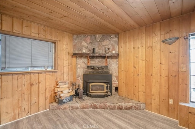 unfurnished living room featuring wooden walls, wood ceiling, a wood stove, and wood finished floors