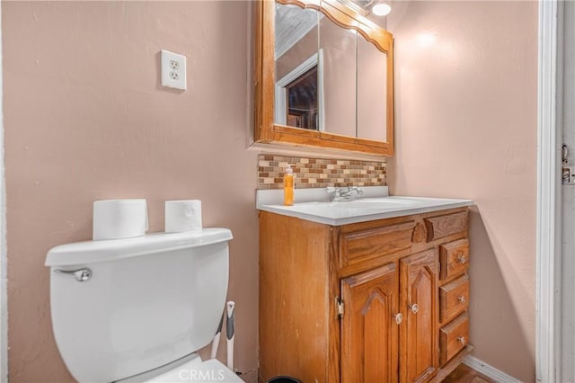 half bathroom with decorative backsplash, baseboards, toilet, and vanity