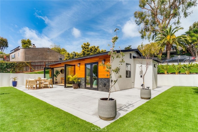 rear view of house with fence, stone siding, french doors, a patio area, and a lawn