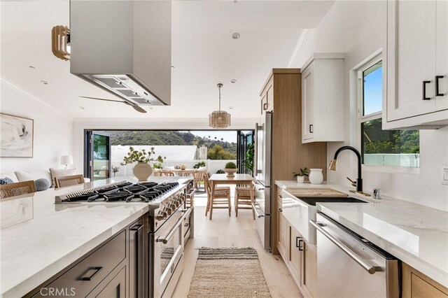 kitchen with decorative light fixtures, appliances with stainless steel finishes, light stone countertops, a sink, and light wood finished floors