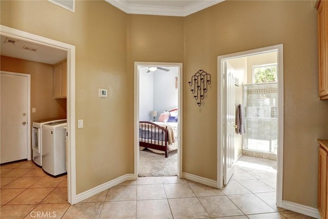 hallway featuring visible vents, baseboards, ornamental molding, light tile patterned flooring, and washer and dryer