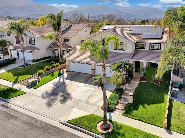 traditional-style home with a front yard, a mountain view, solar panels, a tiled roof, and driveway