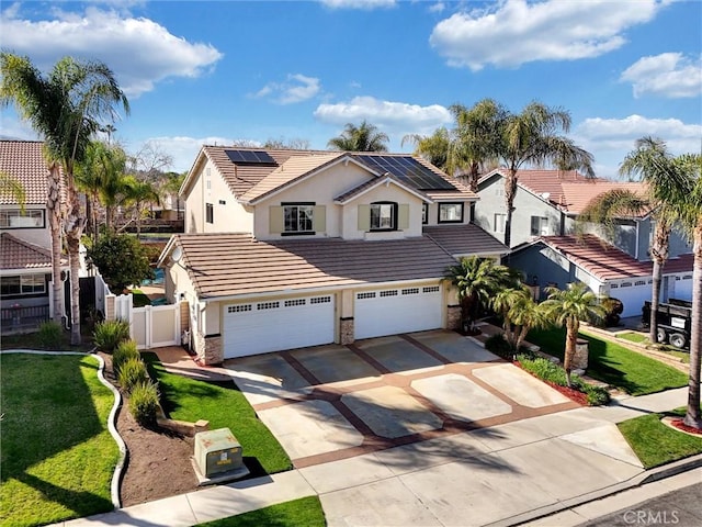 traditional-style home with fence, roof mounted solar panels, a tiled roof, an attached garage, and driveway