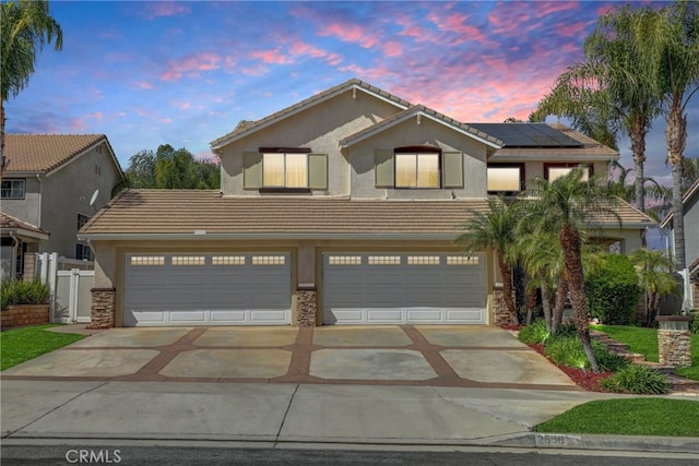 traditional home featuring a tiled roof, driveway, roof mounted solar panels, and stucco siding