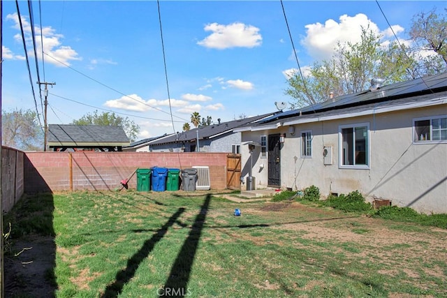 rear view of property with a fenced backyard, solar panels, a yard, and stucco siding