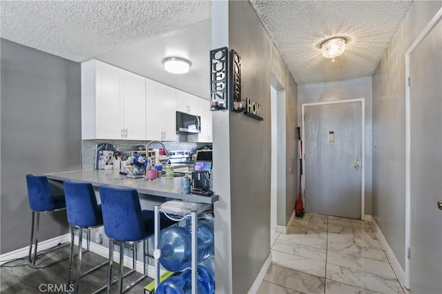 kitchen with appliances with stainless steel finishes, marble finish floor, baseboards, a textured ceiling, and a kitchen breakfast bar