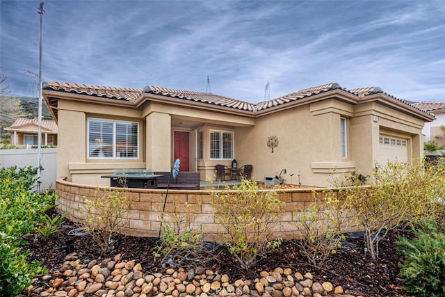 mediterranean / spanish-style home featuring an attached garage, a tiled roof, stucco siding, and fence