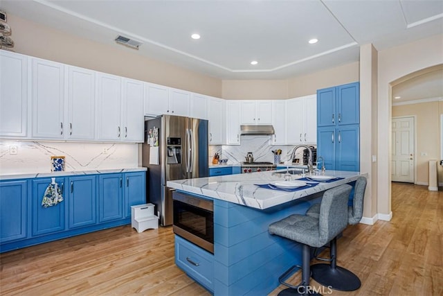 kitchen with a kitchen breakfast bar, blue cabinetry, under cabinet range hood, appliances with stainless steel finishes, and light wood finished floors