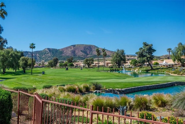 view of community with a yard, a water and mountain view, fence, and view of golf course
