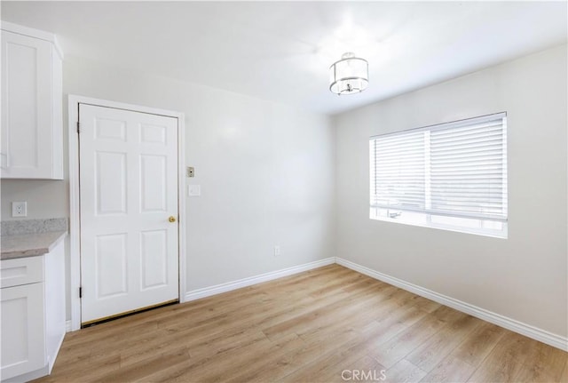 unfurnished dining area featuring a chandelier, baseboards, and light wood-style floors