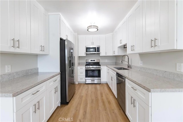 kitchen featuring a sink, white cabinetry, light wood-style flooring, appliances with stainless steel finishes, and light stone countertops