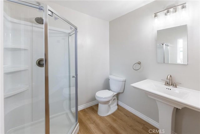 bathroom with baseboards, wood finished floors, toilet, and a stall shower