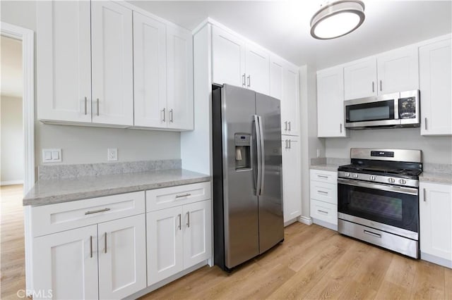 kitchen with light wood-style flooring, light stone counters, white cabinetry, and appliances with stainless steel finishes
