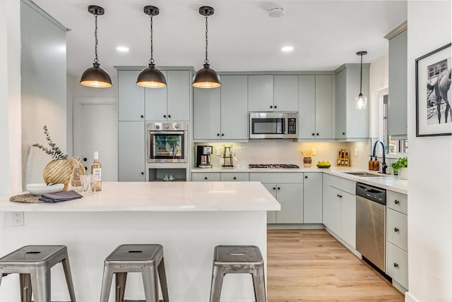 kitchen featuring a breakfast bar area, light countertops, a peninsula, stainless steel appliances, and a sink