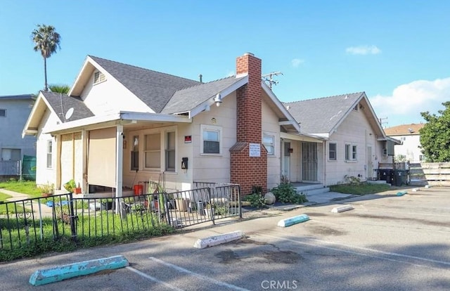 bungalow with fence, roof with shingles, and a chimney
