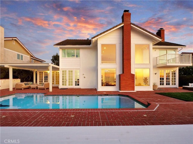 49 Country Ln, Rolling Hills Estates, CA 90274 - back of property at dusk featuring an outdoor pool, a chimney, french doors, a balcony, and a patio area