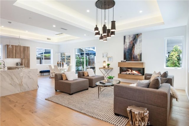 living room with a raised ceiling, visible vents, light wood-type flooring, and a lit fireplace