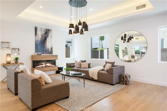 living area featuring a tray ceiling, visible vents, light wood finished floors, and a multi sided fireplace