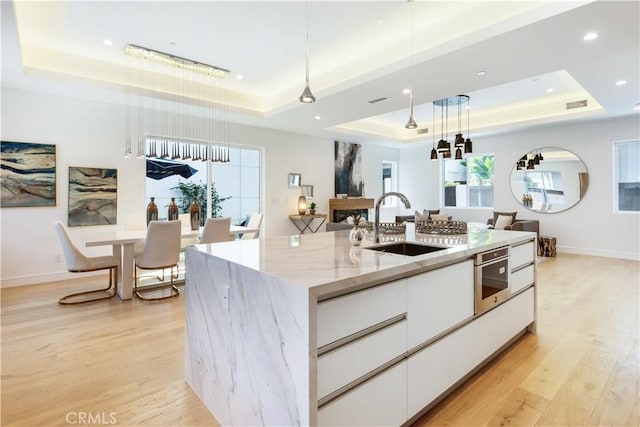 kitchen with a sink, a tray ceiling, light wood-style flooring, white cabinetry, and modern cabinets