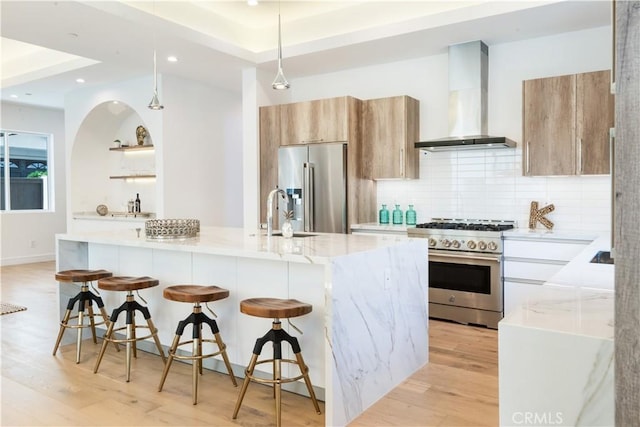 kitchen with tasteful backsplash, wall chimney range hood, high quality appliances, light stone counters, and a sink