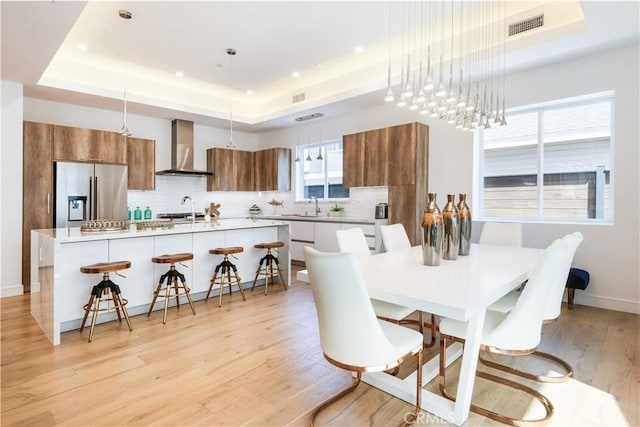 dining area with a tray ceiling, baseboards, visible vents, and light wood-style flooring