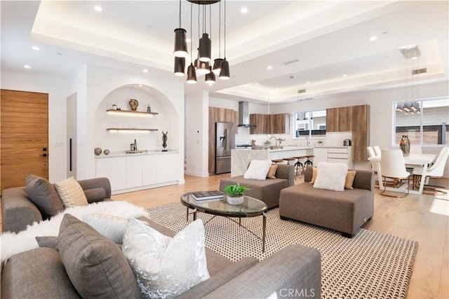 living area with a tray ceiling, recessed lighting, light wood-type flooring, and a chandelier