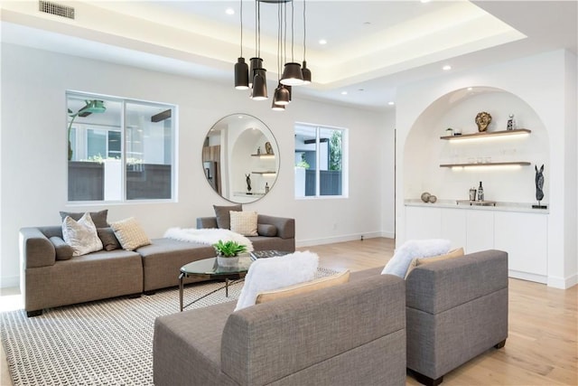 living room with visible vents, recessed lighting, light wood-style floors, a raised ceiling, and a notable chandelier