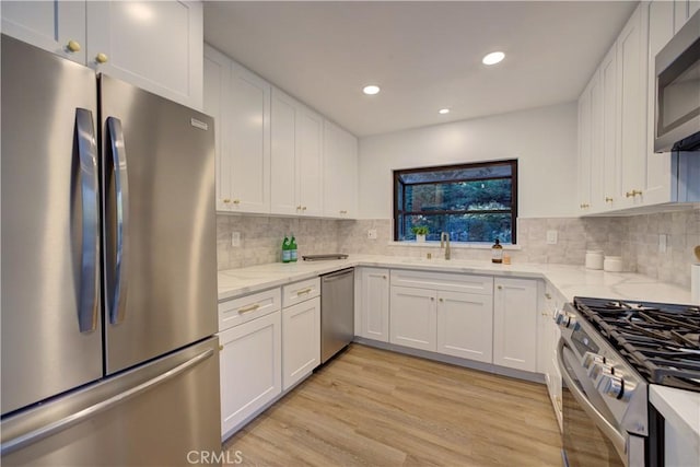 kitchen featuring light stone counters, a sink, white cabinets, light wood-style floors, and appliances with stainless steel finishes