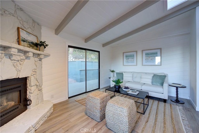 living room featuring a stone fireplace, lofted ceiling with beams, baseboards, and wood finished floors