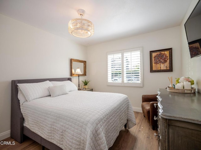 bedroom featuring a notable chandelier, baseboards, and light wood-style floors