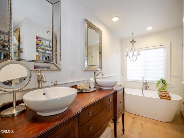 full bath featuring a soaking tub, wood finished floors, double vanity, and a sink
