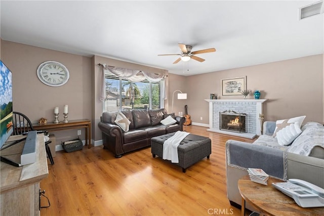 living room with a ceiling fan, visible vents, a brick fireplace, baseboards, and light wood-style floors