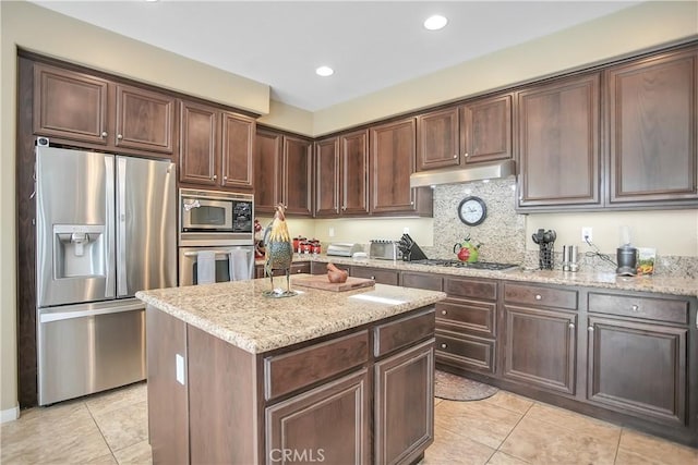 31973 Wildwood Ct, Temecula, CA 92592 - kitchen featuring appliances with stainless steel finishes, under cabinet range hood, light tile patterned floors, light stone counters, and a center island
