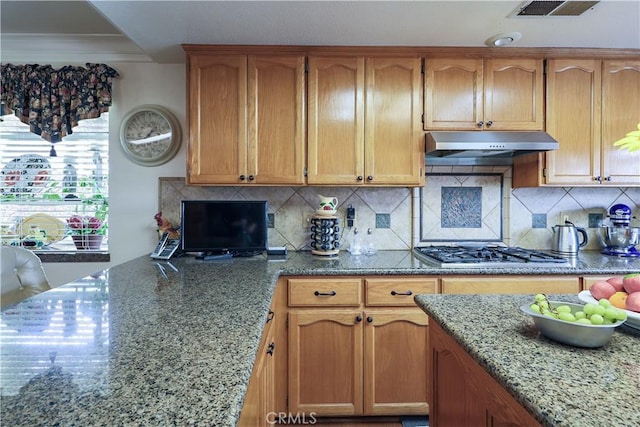 kitchen with under cabinet range hood, decorative backsplash, light stone countertops, and stainless steel gas stovetop