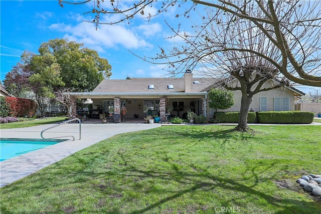 back of property with a yard, a chimney, and a patio area