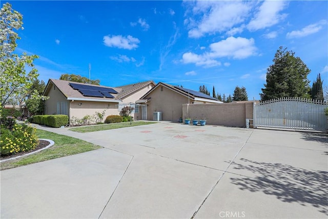 view of home's exterior featuring stucco siding, a gate, roof mounted solar panels, fence, and concrete driveway