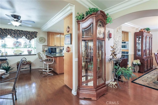 kitchen featuring crown molding, oven, arched walkways, a ceiling fan, and wood-type flooring