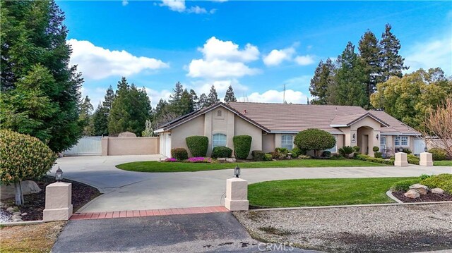 ranch-style home featuring a front yard, a gate, stucco siding, curved driveway, and a tile roof