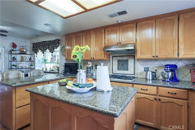 kitchen featuring gas cooktop, brown cabinetry, visible vents, under cabinet range hood, and a center island