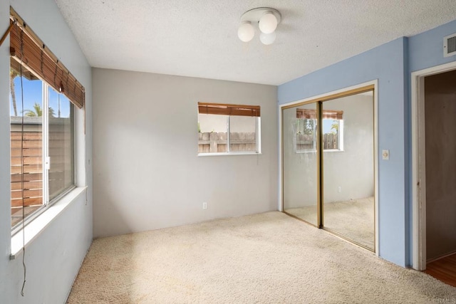 unfurnished bedroom featuring carpet flooring, multiple windows, a textured ceiling, and a closet