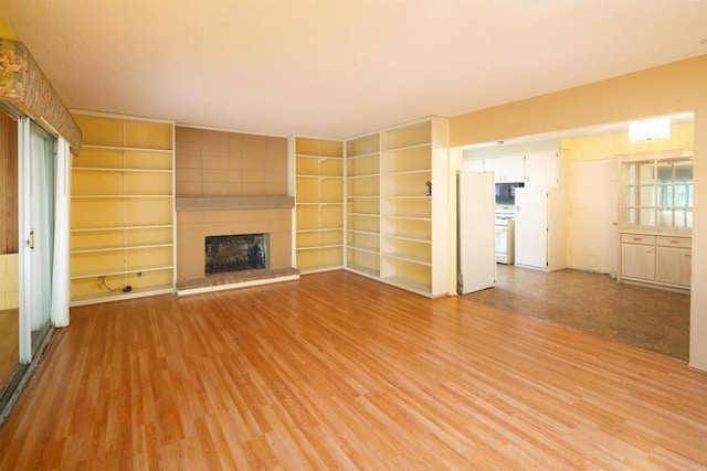unfurnished living room featuring light wood finished floors, a large fireplace, and built in shelves