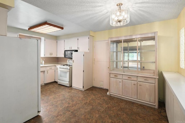 kitchen with an inviting chandelier, a textured ceiling, white appliances, and light countertops