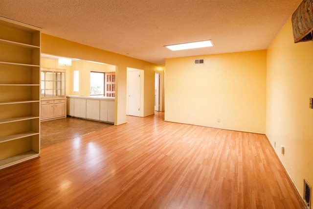 unfurnished living room with a textured ceiling, visible vents, and wood finished floors