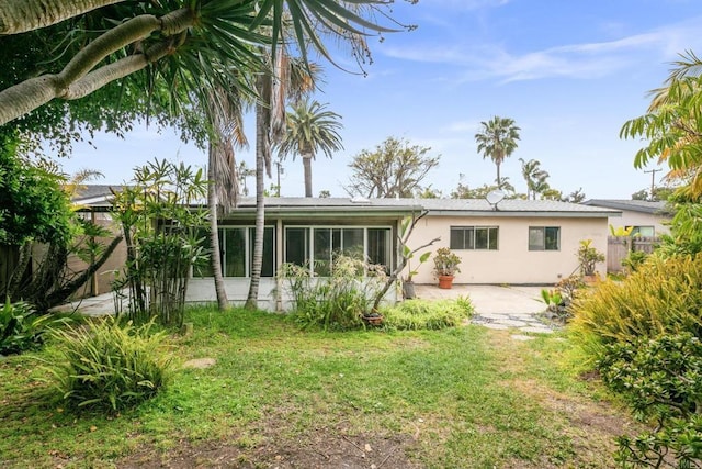 back of property with fence, a patio area, a yard, stucco siding, and a sunroom