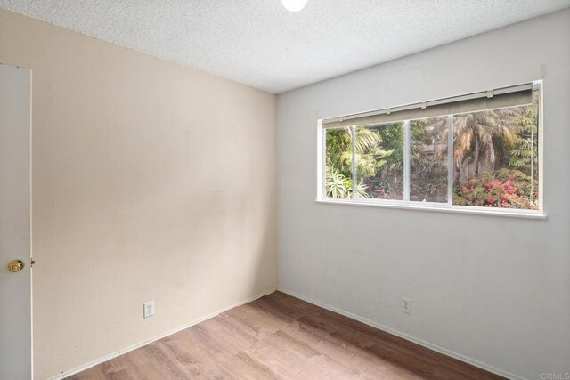 unfurnished room featuring baseboards, a textured ceiling, and wood finished floors