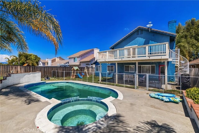 view of swimming pool with a pool with connected hot tub, a wooden deck, a fenced backyard, and a playground
