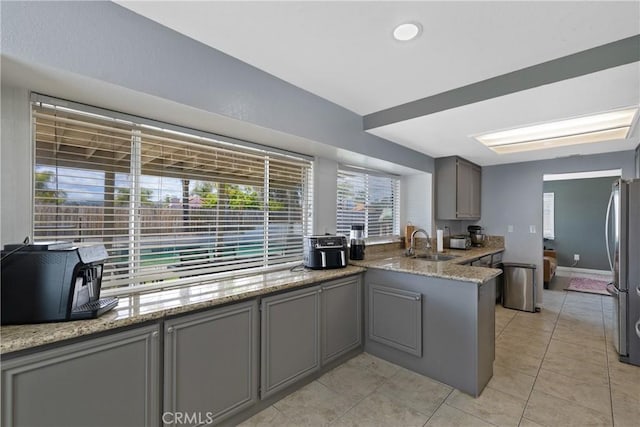kitchen with freestanding refrigerator, a peninsula, a sink, light tile patterned floors, and gray cabinetry